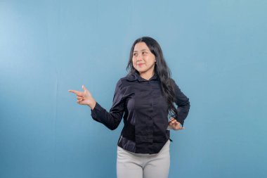 Bir kadın parmağıyla bir şeyi işaret ediyor. O, siyah bir gömlek ve beyaz pantolon giyiyor. Gülümsüyor ve mutlu.