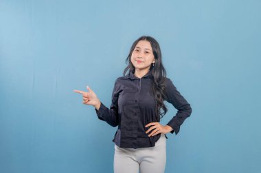 Bir kadın parmağıyla bir şeyi işaret ediyor. O, siyah bir gömlek ve beyaz pantolon giyiyor. Gülümsüyor ve mutlu.