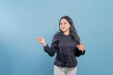 Bir kadın parmağıyla bir şeyi işaret ediyor. O, siyah bir gömlek ve beyaz pantolon giyiyor. Gülümsüyor ve mutlu.