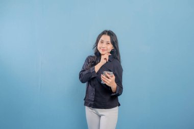 Bir kadın mavi bir duvarın önünde duruyor, elindeki tablete bakıyor. Derin düşüncelere dalmış, muhtemelen bir karar ya da sorun düşünüyor.