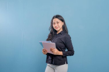 Bir kadın bir yığın kitap tutuyor ve gülümsüyor. O, siyah bir gömlek ve beyaz pantolon giyiyor. Güven ve pozitiflik kavramı