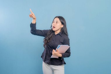 Bir kadın elinde bir yığın kitap tutarken bir şeyi işaret ediyor. Kadın muhtemelen bir mesaj iletmeye ya da biriyle bilgi paylaşmaya çalıştığı için önem ve odaklanma kavramı.