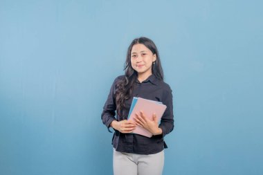 Bir kadın bir yığın kitap tutuyor ve gülümsüyor. O, siyah bir gömlek ve beyaz pantolon giyiyor. Güven ve pozitiflik kavramı