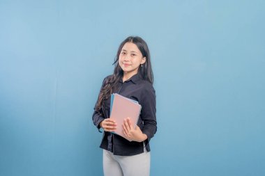 Bir kadın bir yığın kitap tutuyor ve gülümsüyor. O, siyah bir gömlek ve beyaz pantolon giyiyor. Güven ve pozitiflik kavramı