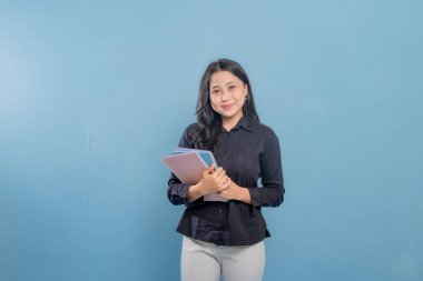 Bir kadın bir yığın kitap tutuyor ve gülümsüyor. O, siyah bir gömlek ve beyaz pantolon giyiyor. Güven ve pozitiflik kavramı