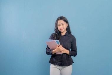 Bir kadın bir yığın kitap tutuyor ve gülümsüyor. O, siyah bir gömlek ve beyaz pantolon giyiyor. Güven ve pozitiflik kavramı