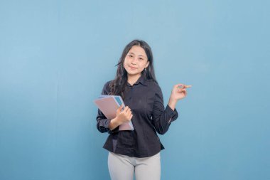 Bir kadın elinde bir yığın kitap ya da kağıt tutarken bir şeyi işaret ediyor. O, siyah bir gömlek ve beyaz pantolon giyiyor. Önem kavramı ve odak