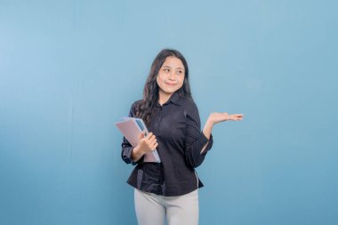 Bir kadın elinde üç kitap tutuyor ve önemli bir şeye işaret ediyor. Gülümsüyor ve mutlu.