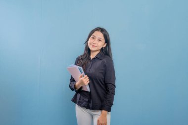 Bir kadın bir yığın kitap tutuyor ve gülümsüyor. O, siyah bir gömlek ve beyaz pantolon giyiyor. Güven ve pozitiflik kavramı