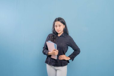 Bir kadın bir yığın kitap tutuyor ve gülümsüyor. O, siyah bir gömlek ve beyaz pantolon giyiyor. Güven ve pozitiflik kavramı