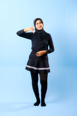 Siyah etek ve siyah pantolon giyen bir kadın. Başparmağıyla işaret ediyor.