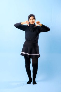 Siyah etek ve siyah pantolon giyen bir kadın. Başparmağıyla işaret ediyor.