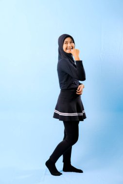 Siyah etek ve siyah pantolon giyen bir kadın. Gülümsüyor ve elleri kalçasında.