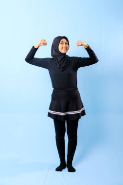 Siyah etekli ve siyah pantolonlu bir kadın fotoğraf için poz veriyor. Gülümsüyor ve kolunu esnetiyor.