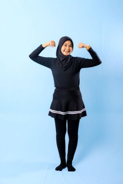 Siyah etekli ve siyah pantolonlu bir kadın fotoğraf için poz veriyor. Gülümsüyor ve kolunu esnetiyor.