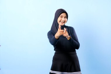 Siyah etek ve siyah başörtüsü takan bir kadın. Bir şeyi işaret ediyor. Gülümsüyor.