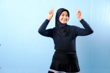 Siyah etek ve siyah başörtüsü takan bir kadın. Bir şeyi işaret ediyor. Gülümsüyor.