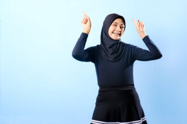 Siyah etek ve siyah başörtüsü takan bir kadın. Bir şeyi işaret ediyor. Gülümsüyor.