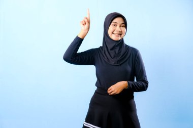 Siyah etek ve siyah başörtüsü takan bir kadın. Bir şeyi işaret ediyor. Gülümsüyor.