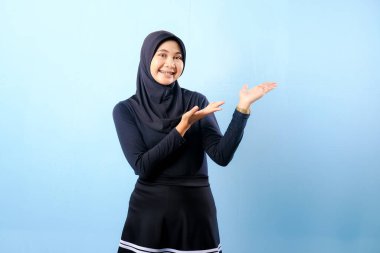 Siyah etek ve siyah başörtüsü takan bir kadın. Bir şeyi işaret ediyor. Gülümsüyor.