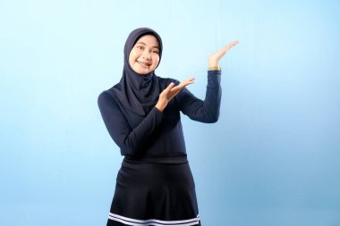 Siyah etek ve siyah başörtüsü takan bir kadın. Bir şeyi işaret ediyor. Gülümsüyor.