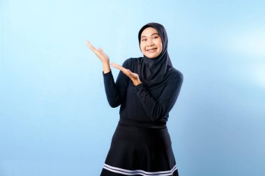 Siyah etek ve siyah başörtüsü takan bir kadın. Bir şeyi işaret ediyor. Gülümsüyor.