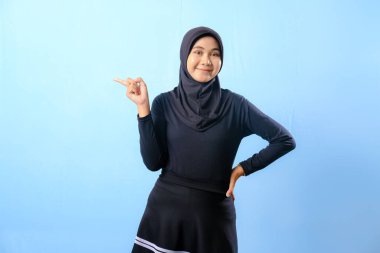 Siyah etek ve siyah başörtüsü takan bir kadın. Bir şeyi işaret ediyor. Gülümsüyor.