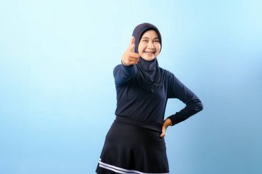 Siyah etek ve siyah başörtüsü takan bir kadın. Bir şeyi işaret ediyor. Gülümsüyor.