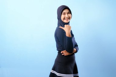 Siyah etek ve siyah başörtüsü takan bir kadın. Bir şeyi işaret ediyor. Gülümsüyor.