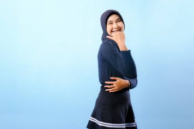 Siyah etek ve siyah başörtüsü takan bir kadın. Bir şeyi işaret ediyor. Gülümsüyor.