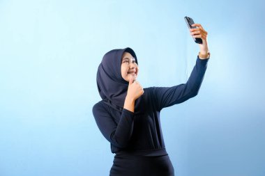 Siyah tesettürlü bir kadın cep telefonuyla selfie çekiyor. Gülümsüyor ve mutlu.