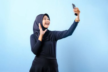 Siyah tesettürlü bir kadın cep telefonuyla selfie çekiyor. Gülümsüyor ve mutlu.