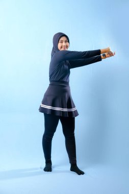 Siyah elbiseli bir kadın kollarını yana doğru açıyor. Siyah çorap ve siyah pantolon giyiyor.