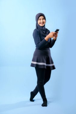 Siyah etek ve siyah pantolon giyen bir kadın cep telefonu tutuyor. Gülümsüyor ve mutlu.