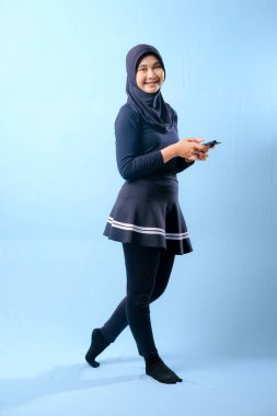 Siyah etek ve siyah pantolon giyen bir kadın cep telefonu tutuyor. Gülümsüyor ve mutlu.