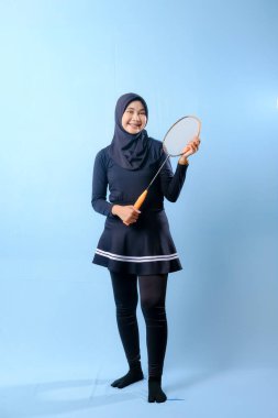 Siyah etekli ve elinde badminton raketi olan siyah pantolonlu bir kadın. Gülümsüyor ve mutlu.