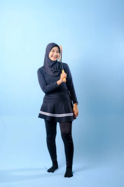 Siyah etekli ve elinde badminton raketi olan siyah pantolonlu bir kadın. Gülümsüyor ve mutlu.