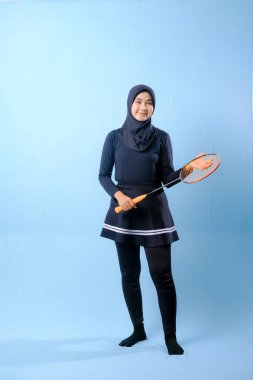 Siyah etekli ve elinde badminton raketi olan siyah pantolonlu bir kadın. Gülümsüyor ve mutlu.
