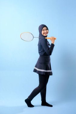 Siyah etekli ve elinde badminton raketi olan siyah pantolonlu bir kadın. Gülümsüyor ve mutlu.