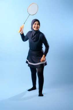 Siyah etekli ve elinde badminton raketi olan siyah pantolonlu bir kadın. Gülümsüyor ve mutlu.