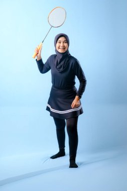 Siyah etekli ve elinde badminton raketi olan siyah pantolonlu bir kadın. Gülümsüyor ve mutlu.