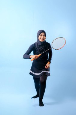 Siyah etekli ve elinde badminton raketi olan siyah pantolonlu bir kadın. Gülümsüyor ve mutlu.