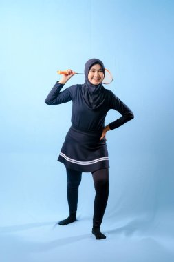 Siyah etekli ve elinde badminton raketi olan siyah pantolonlu bir kadın. Gülümsüyor ve mutlu.