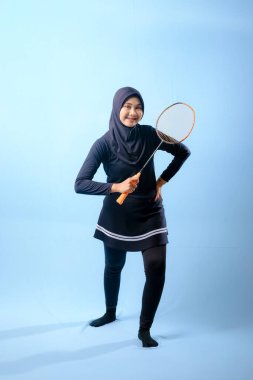 Siyah etekli ve elinde badminton raketi olan siyah pantolonlu bir kadın. Gülümsüyor ve mutlu.