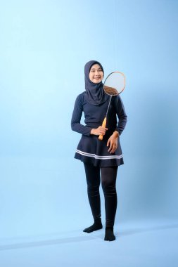 Siyah etekli ve elinde badminton raketi olan siyah pantolonlu bir kadın. Gülümsüyor ve mutlu.