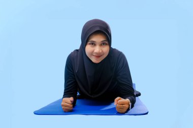 Bir kadın laptopu ve su şişesi olan bir minderde yoga yapıyor. Gülümsüyor ve antrenmanından zevk alıyor.