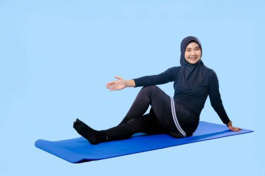 Bir kadın laptopu ve su şişesi olan bir minderde yoga yapıyor. Gülümsüyor ve antrenmanından zevk alıyor.