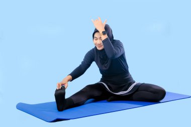 Bir kadın laptopu ve su şişesi olan bir minderde yoga yapıyor. Gülümsüyor ve antrenmanından zevk alıyor.