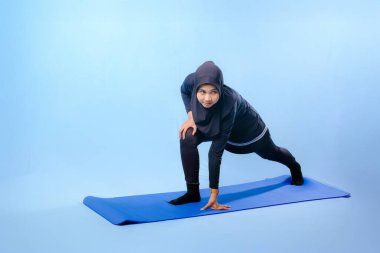 Bir kadın laptopu ve su şişesi olan bir minderde yoga yapıyor. Gülümsüyor ve antrenmanından zevk alıyor.