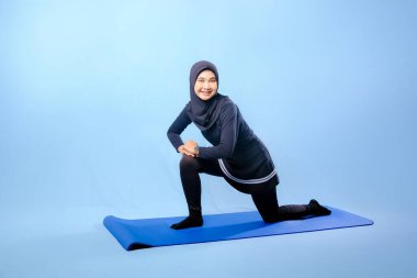 Bir kadın laptopu ve su şişesi olan bir minderde yoga yapıyor. Gülümsüyor ve antrenmanından zevk alıyor.